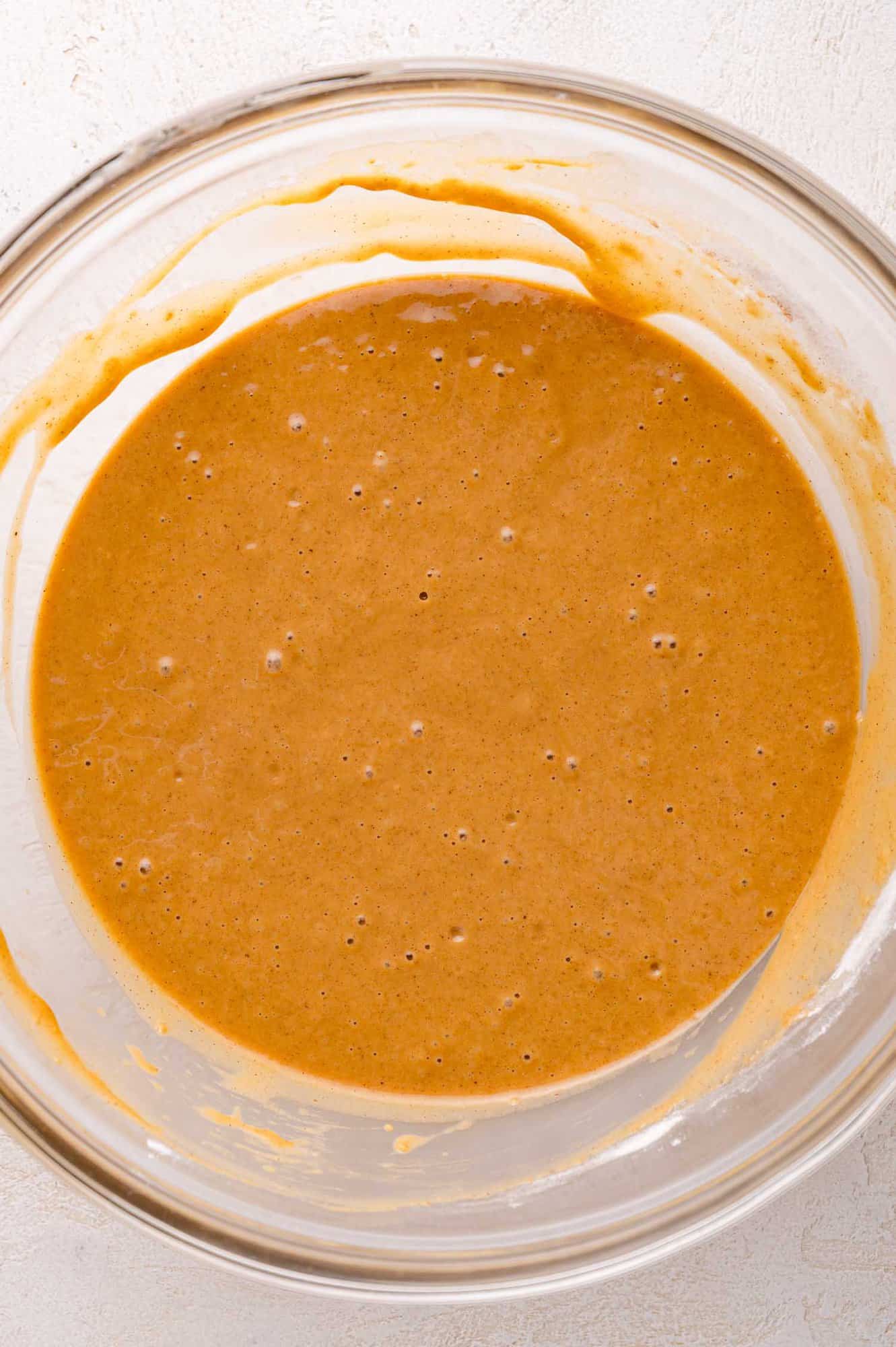 A glass bowl filled with light brown batter, showing a smooth and slightly bubbly surface.