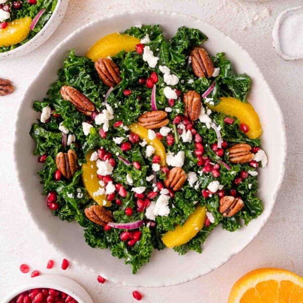 A bowl of kale salad topped with orange slices, pecans, pomegranate seeds, red onion, and crumbled feta cheese.