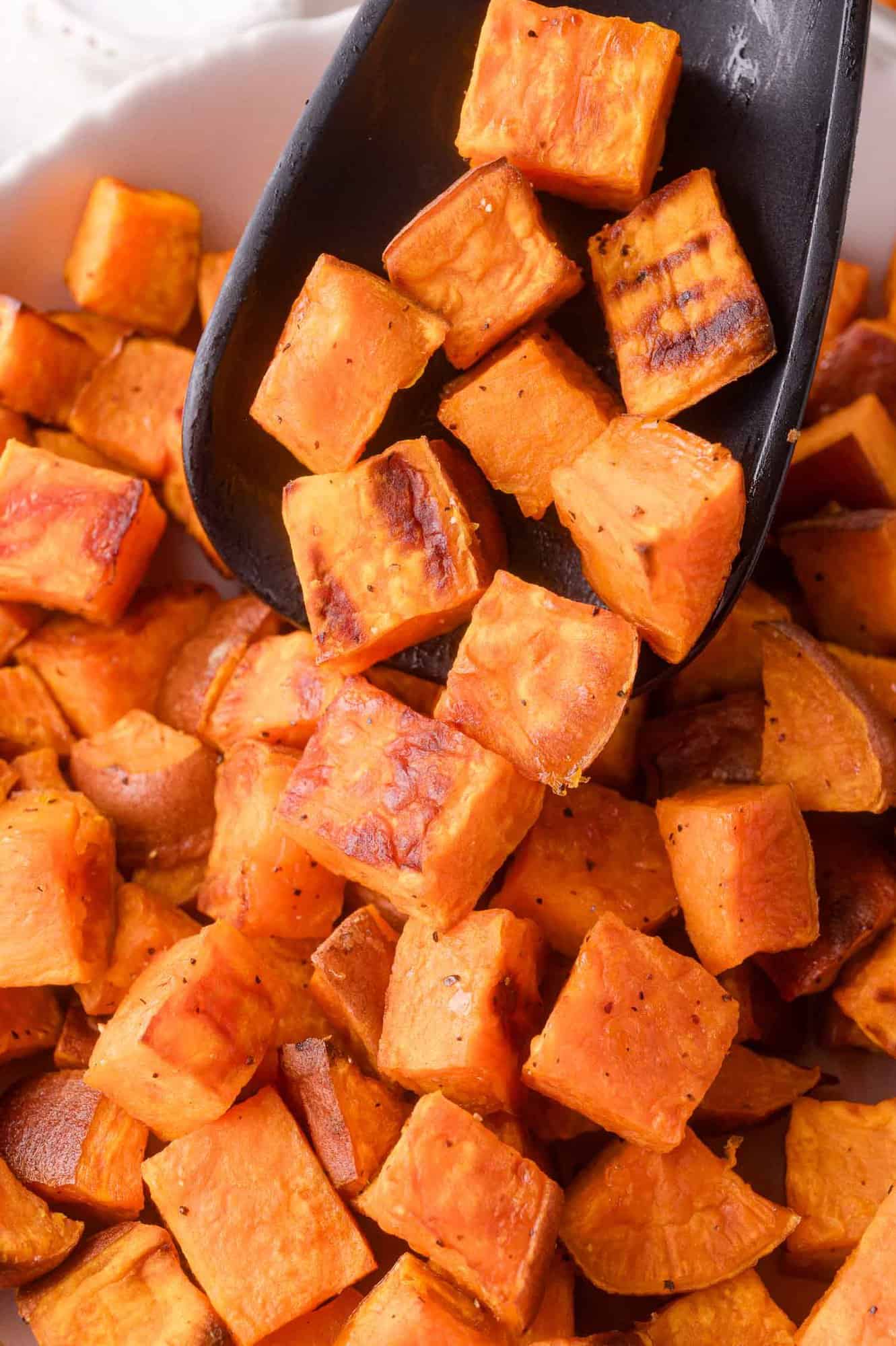 Close-up of roasted sweet potato cubes being scooped with a black spatula.