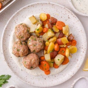 A plate with four meatballs on a white sauce, served with roasted diced potatoes, carrots, and parsnips.