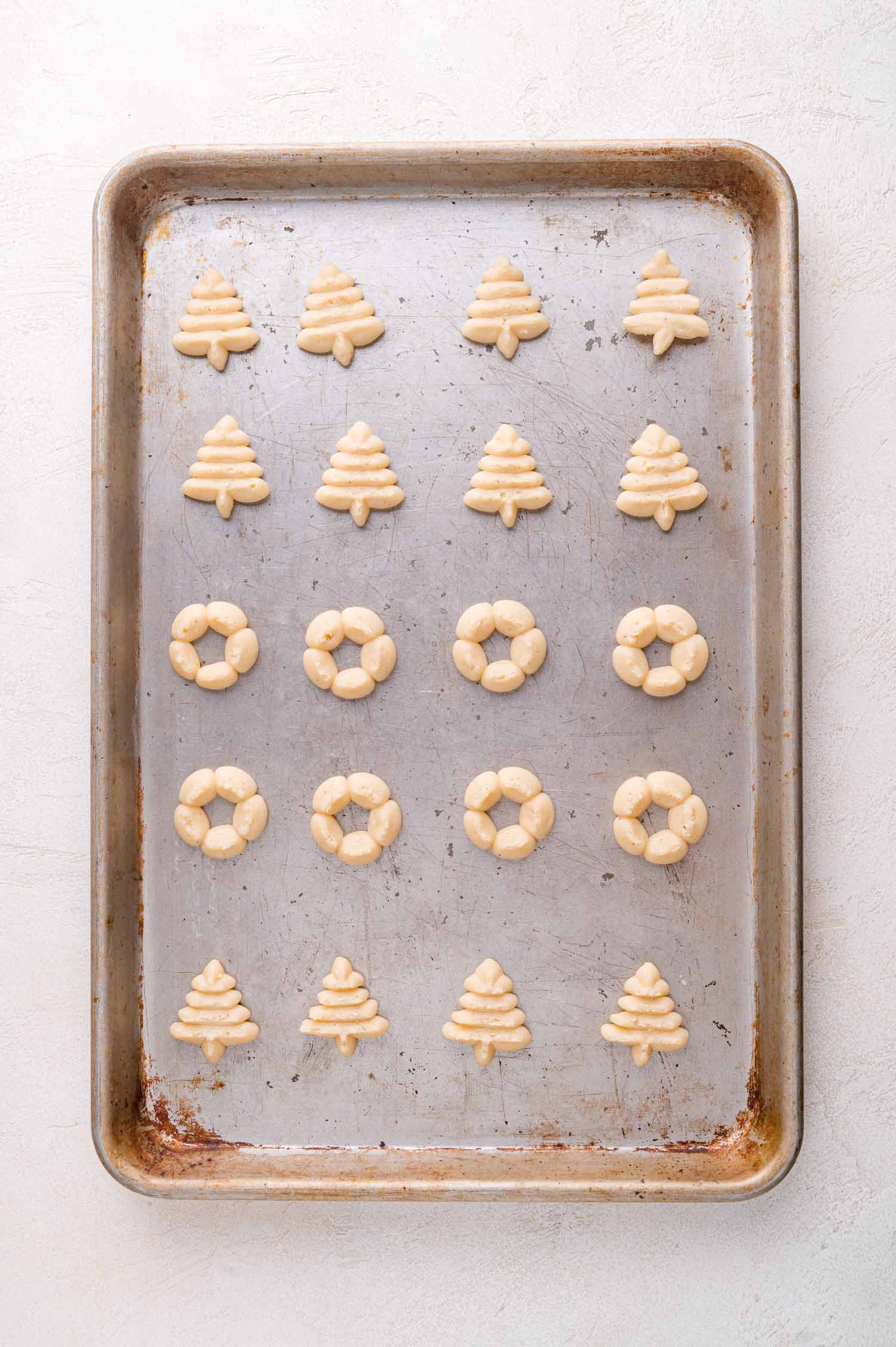 A baking sheet with rows of unbaked Christmas tree and wreath-shaped cookies arranged neatly on it.