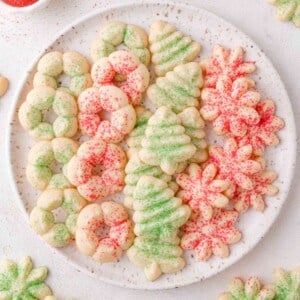 A plate of assorted Christmas cream cheese spritz cookies shaped like wreaths, trees, and snowflakes, decorated with green and red sugar sprinkles.