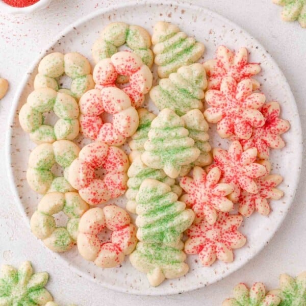 A plate of assorted Christmas cream cheese spritz cookies shaped like wreaths, trees, and snowflakes, decorated with green and red sugar sprinkles.