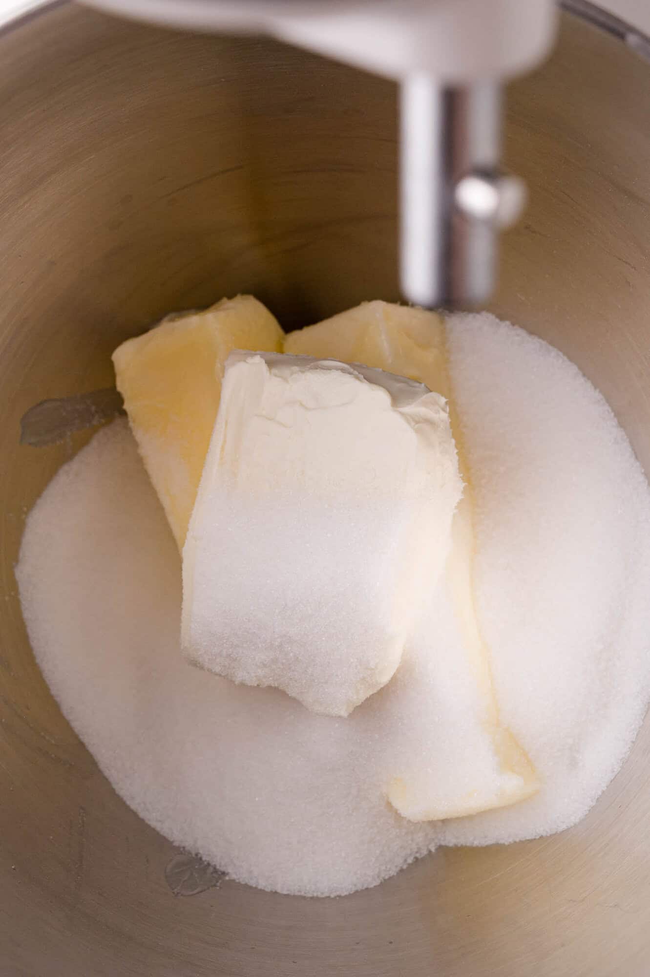 Butter, cream cheese, and granulated sugar in a metal mixing bowl under a stand mixer attachment.