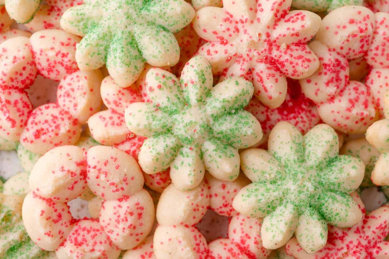A close-up of cream cheese spritz cookies topped with green and red sugar sprinkles, arranged in an overlapping pattern.