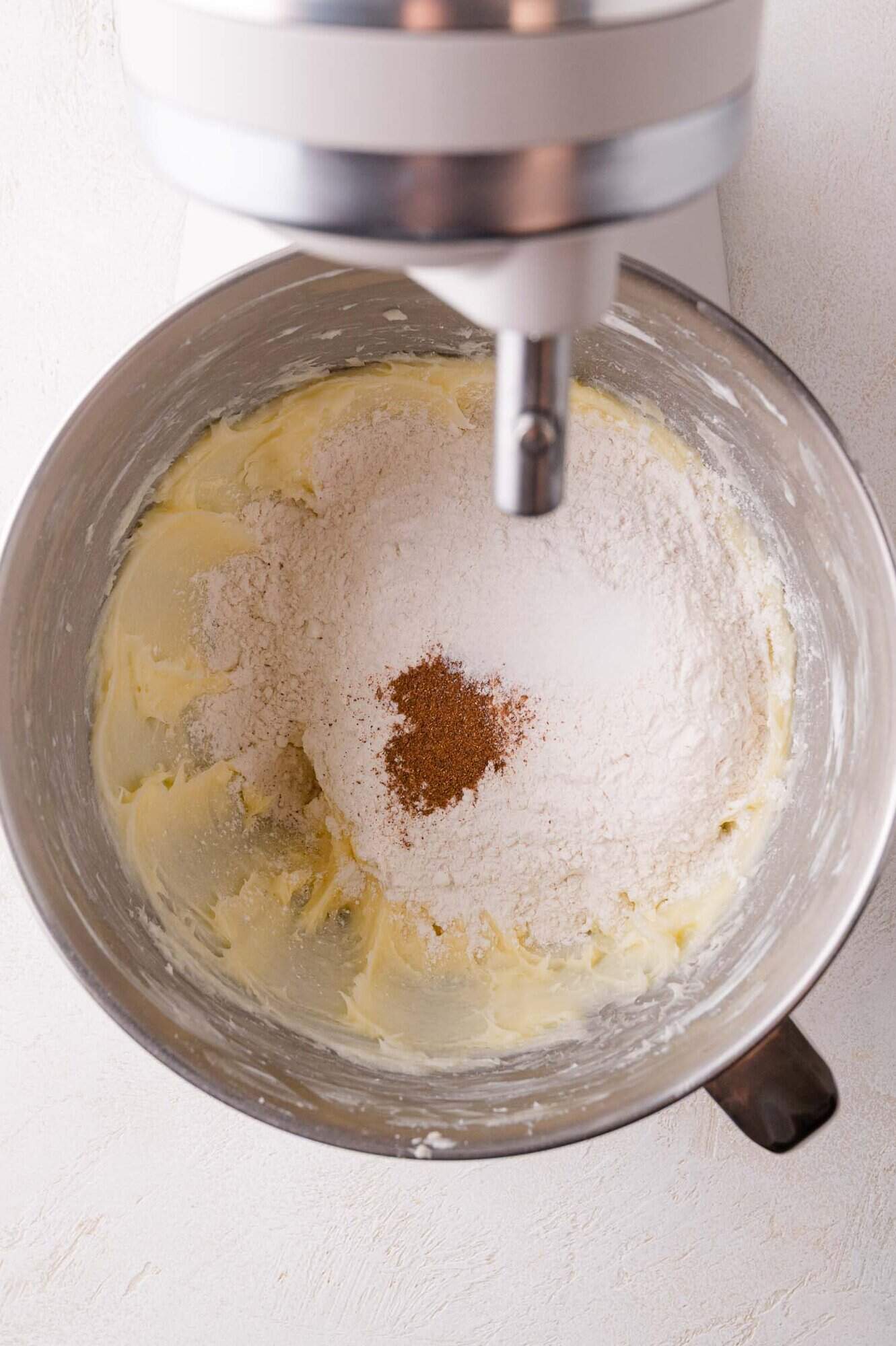 A stand mixer bowl with creamed butter, flour, sugar, and spices ready to be mixed.