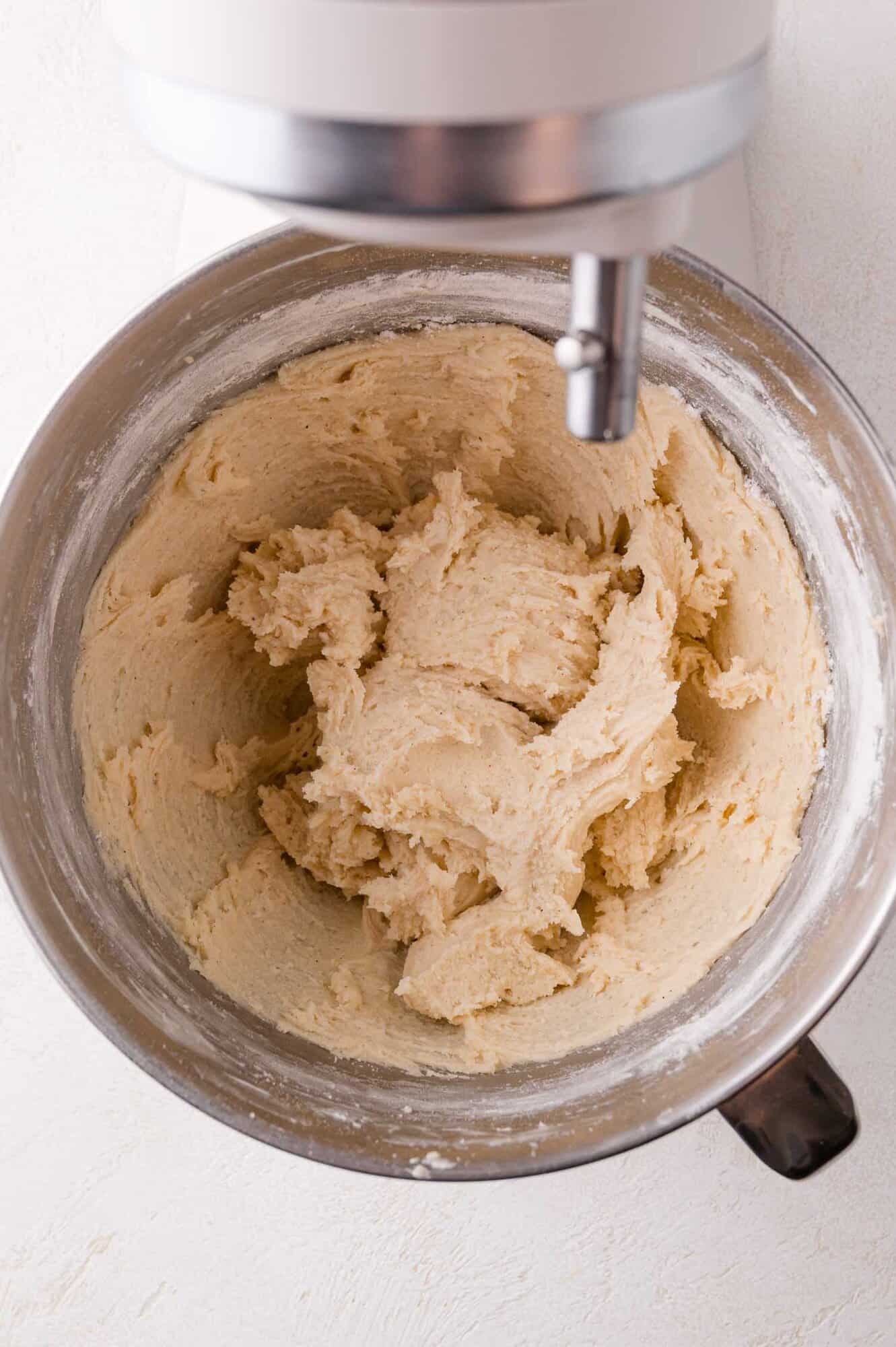 A stand mixer bowl containing creamed cookie dough, viewed from above, with the mixer attachment partially visible at the top.