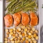 A sheet pan with four ranch seasoned pork chops, roasted green beans at the top, and halved roasted baby potatoes at the bottom.