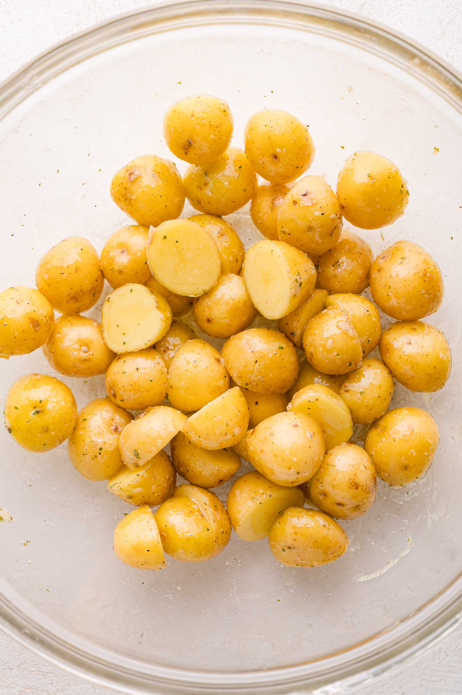 A clear bowl containing halved baby potatoes coated with oil and ranch seasoning.