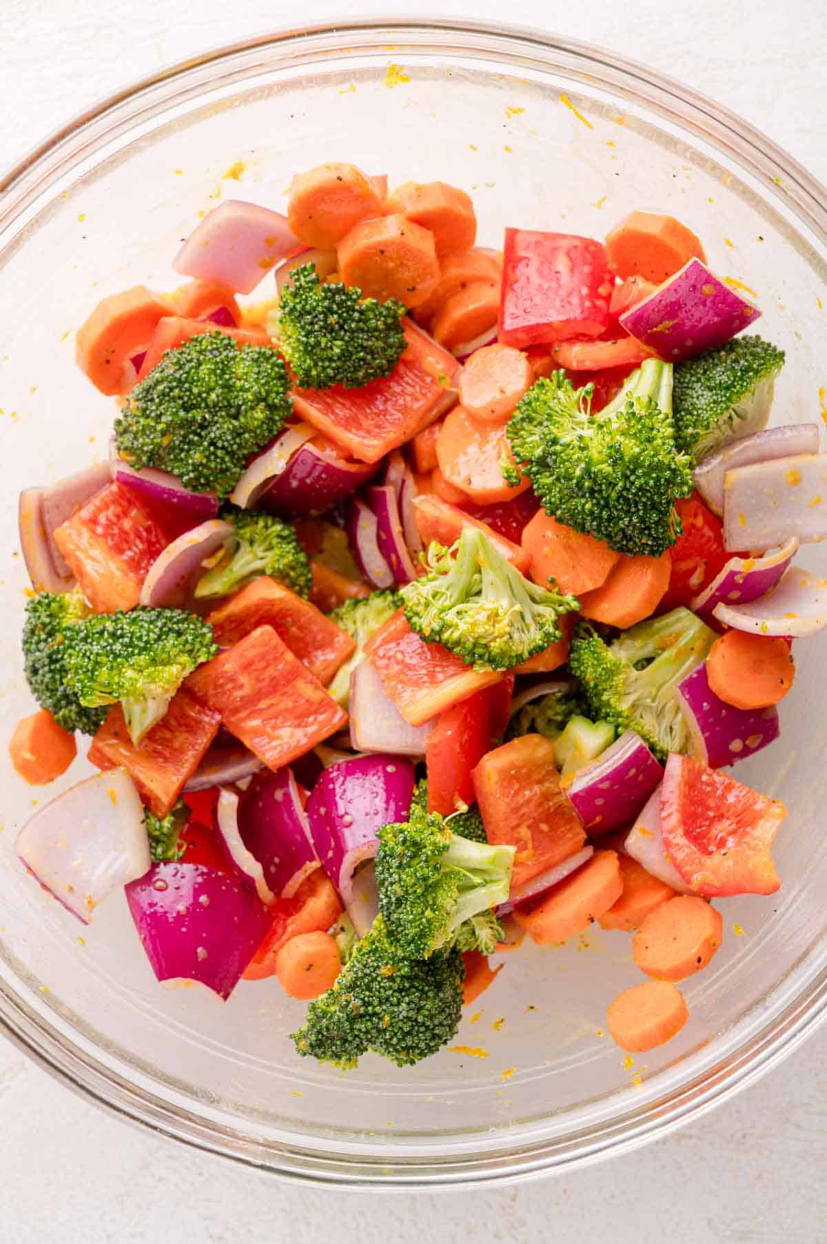 A glass bowl filled with chopped broccoli, red bell pepper, red onion, and carrots.
