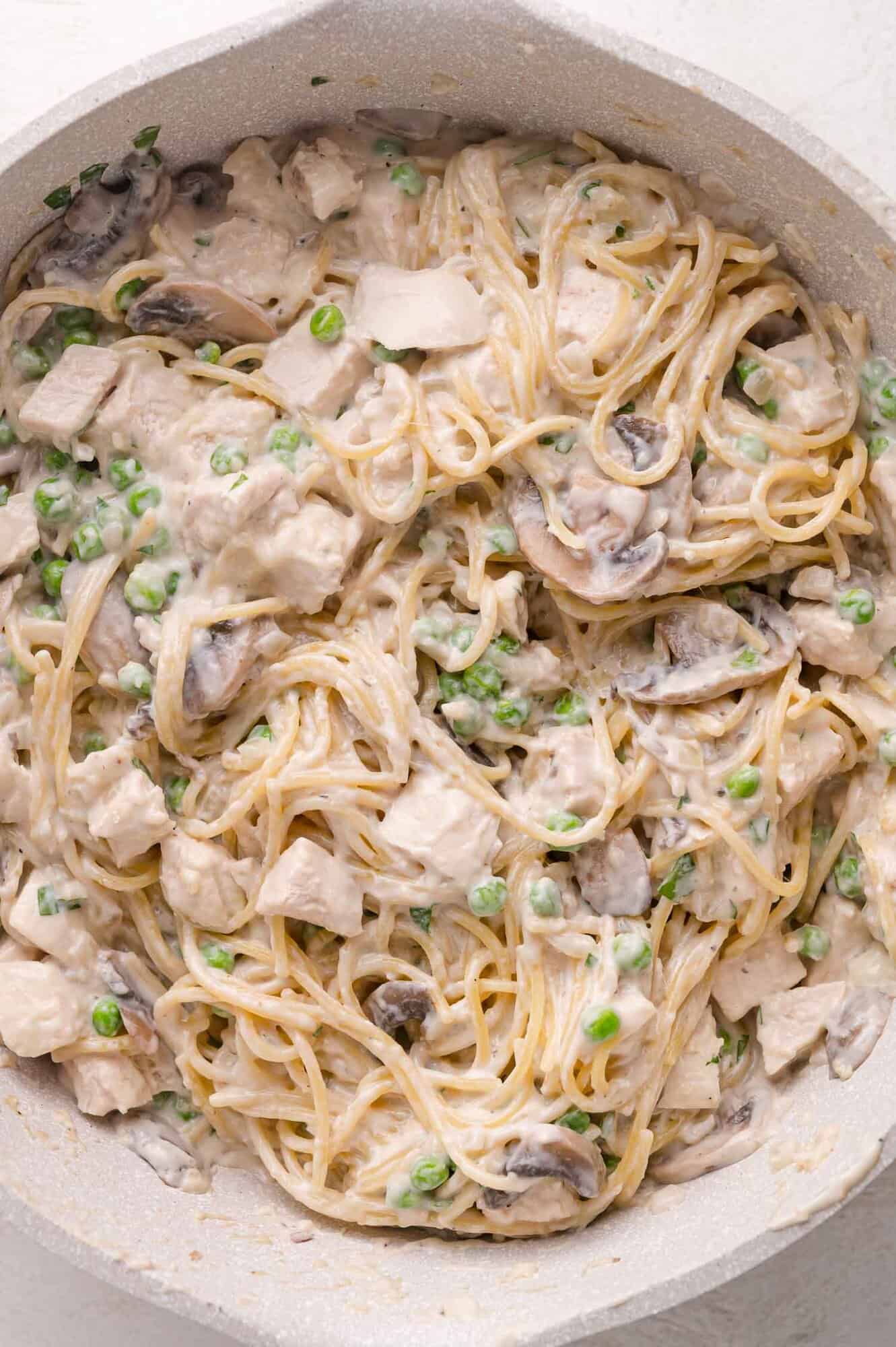 A pan filled with spaghetti mixed with creamy sauce, mushrooms, peas, and pieces of chicken.