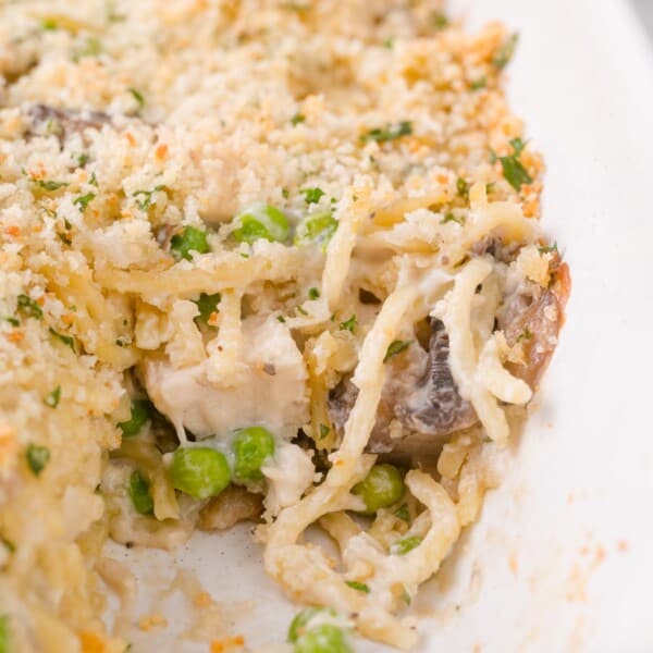 Close-up of a baked chicken tetrazinni casserole featuring spaghetti, peas, mushrooms, chicken, and a breadcrumb topping in a white dish.