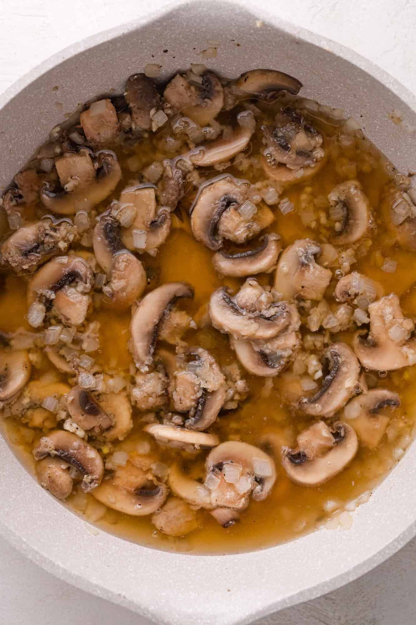 Sliced mushrooms and chopped onions simmering in a pan with broth.