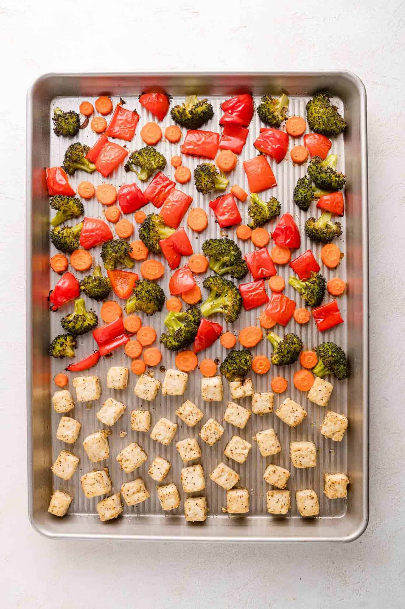 A baking sheet with roasted broccoli, red bell peppers, carrots, and seasoned tofu cubes arranged in separate sections.