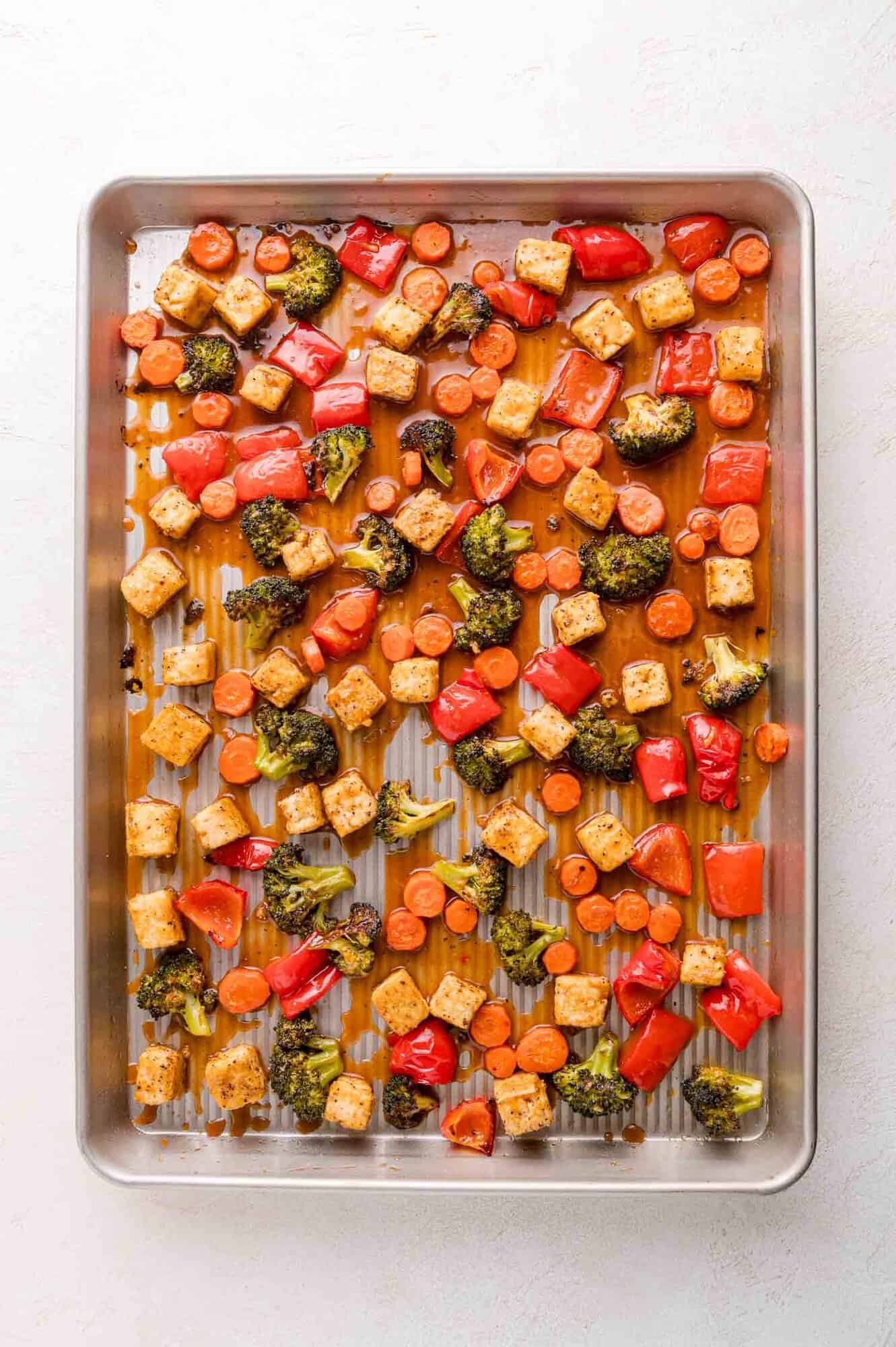 A baking sheet with roasted tofu cubes, broccoli florets, sliced carrots, and red bell pepper pieces.