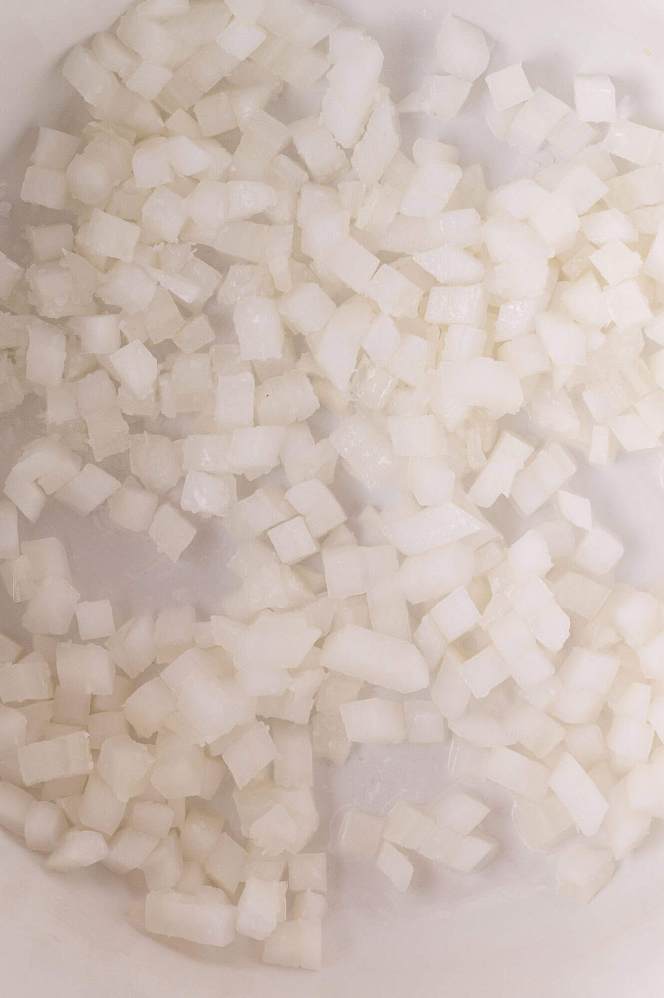 Chopped white onions in a pan, starting to soften as they cook.