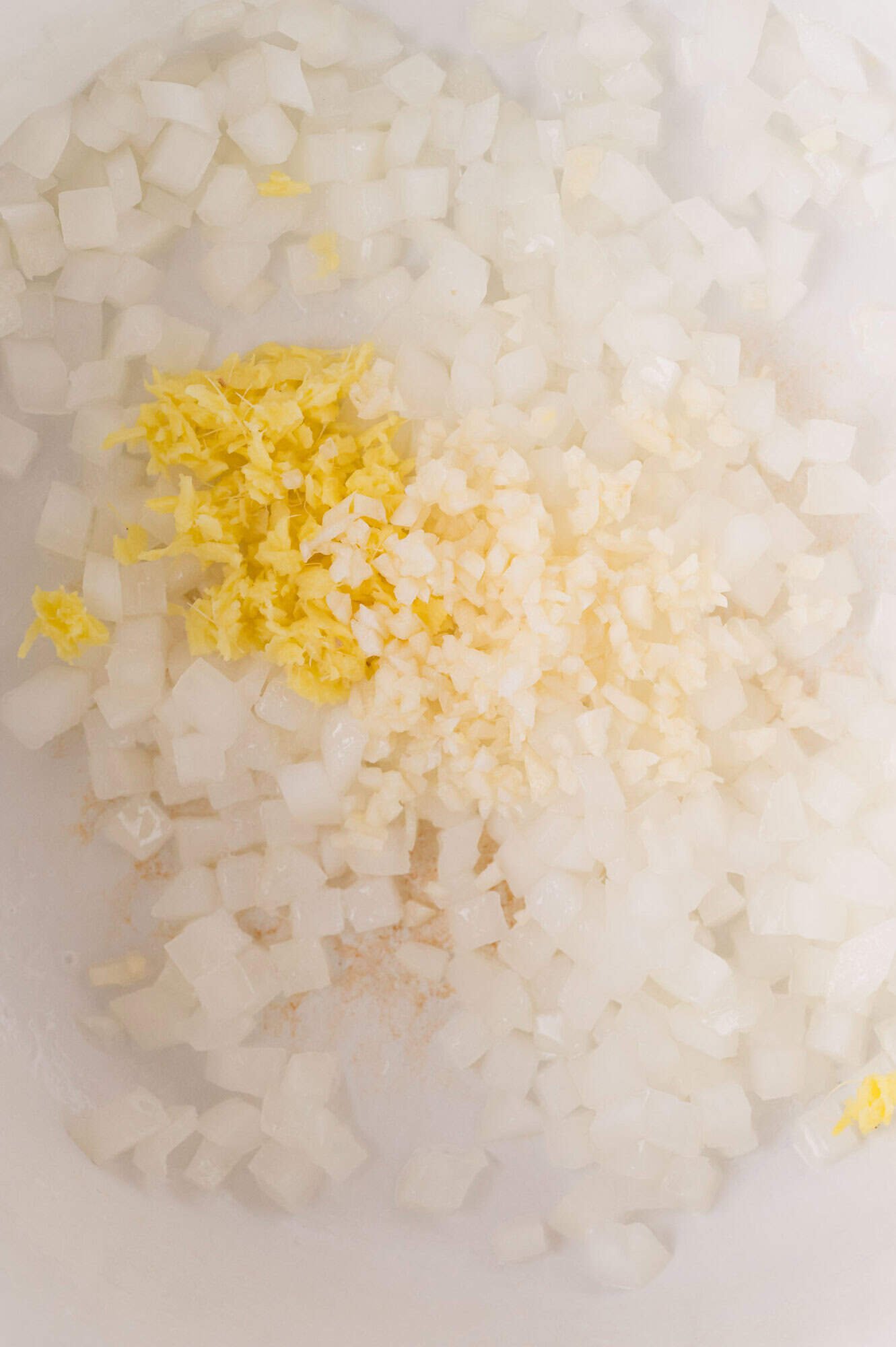 Chopped onions, minced garlic, and grated ginger cooking together in a white pan.