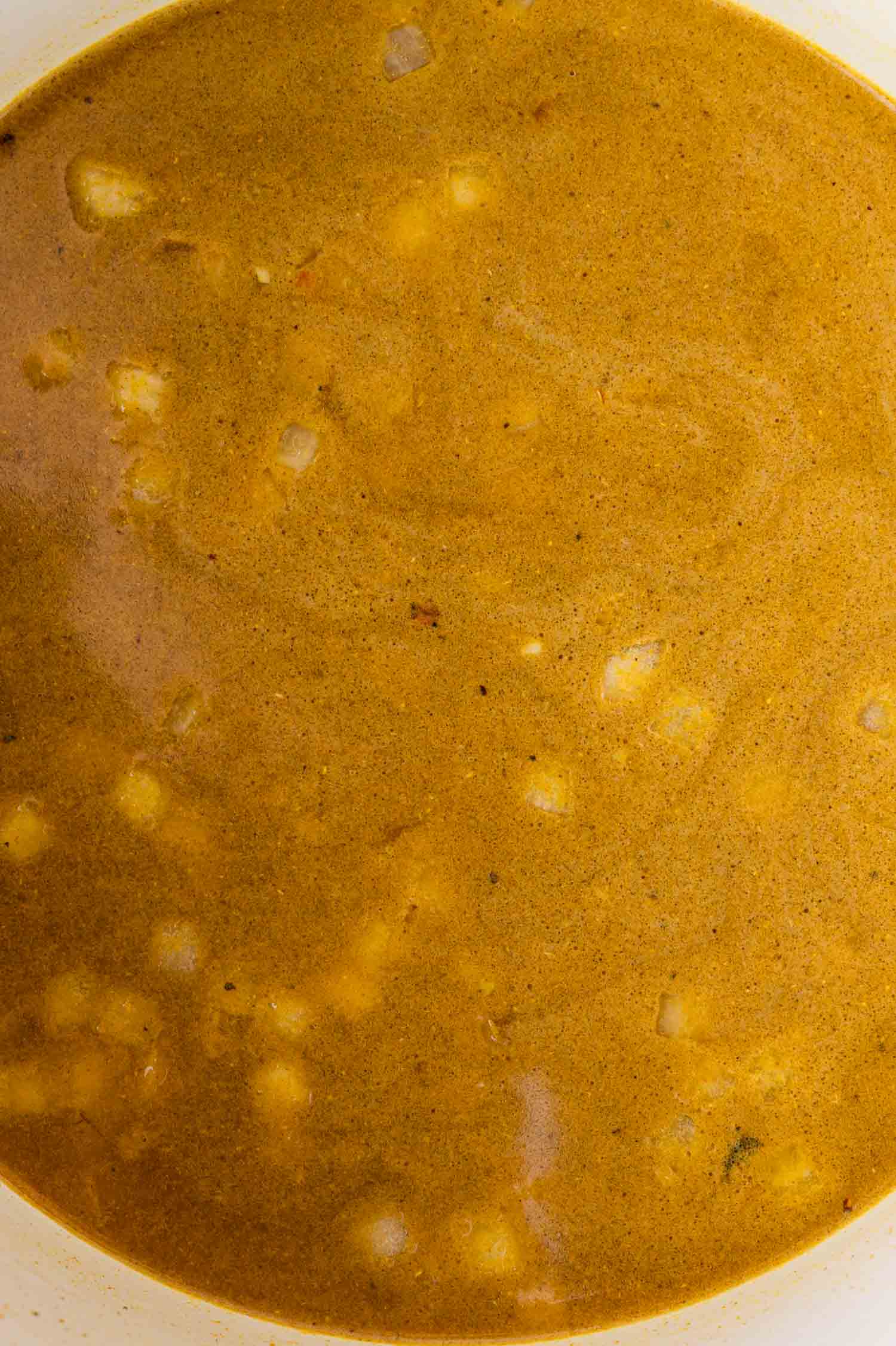 A close-up view of brown-colored broth with small chunks of onion and a smooth, slightly textured surface.