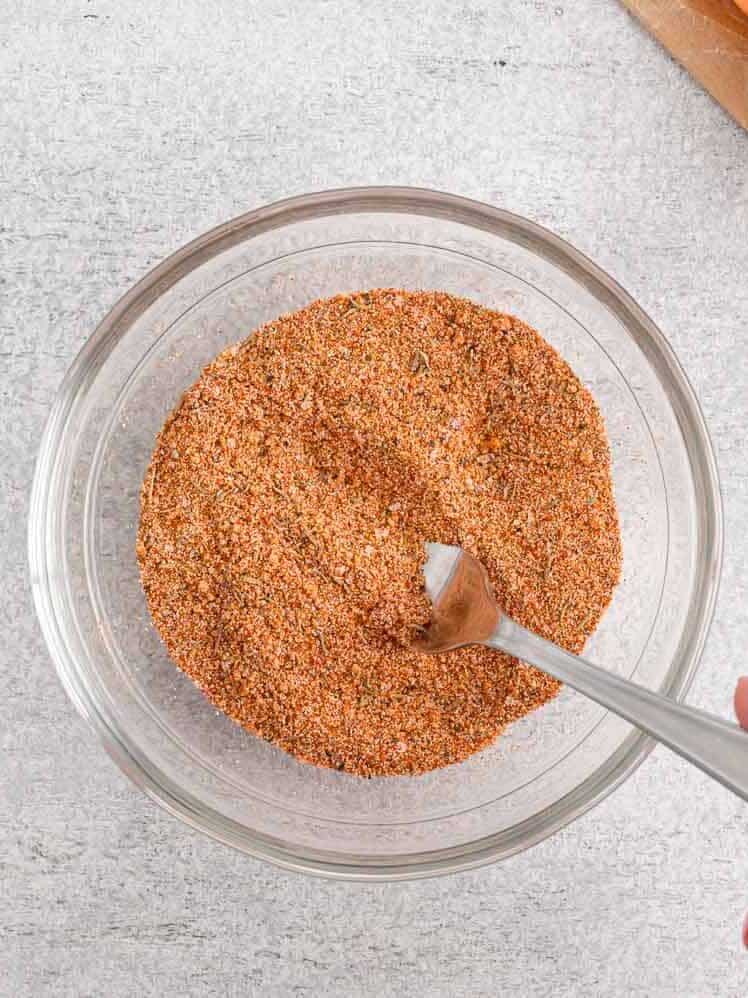 Spices in a small glass bowl, being mixed with a small spoon.
