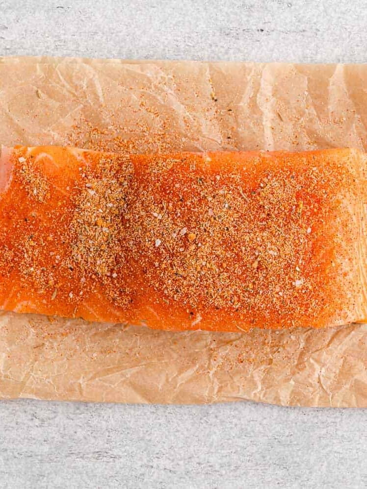 Piece of raw salmon on top of parchment paper, sprinkled with salmon seasoning.