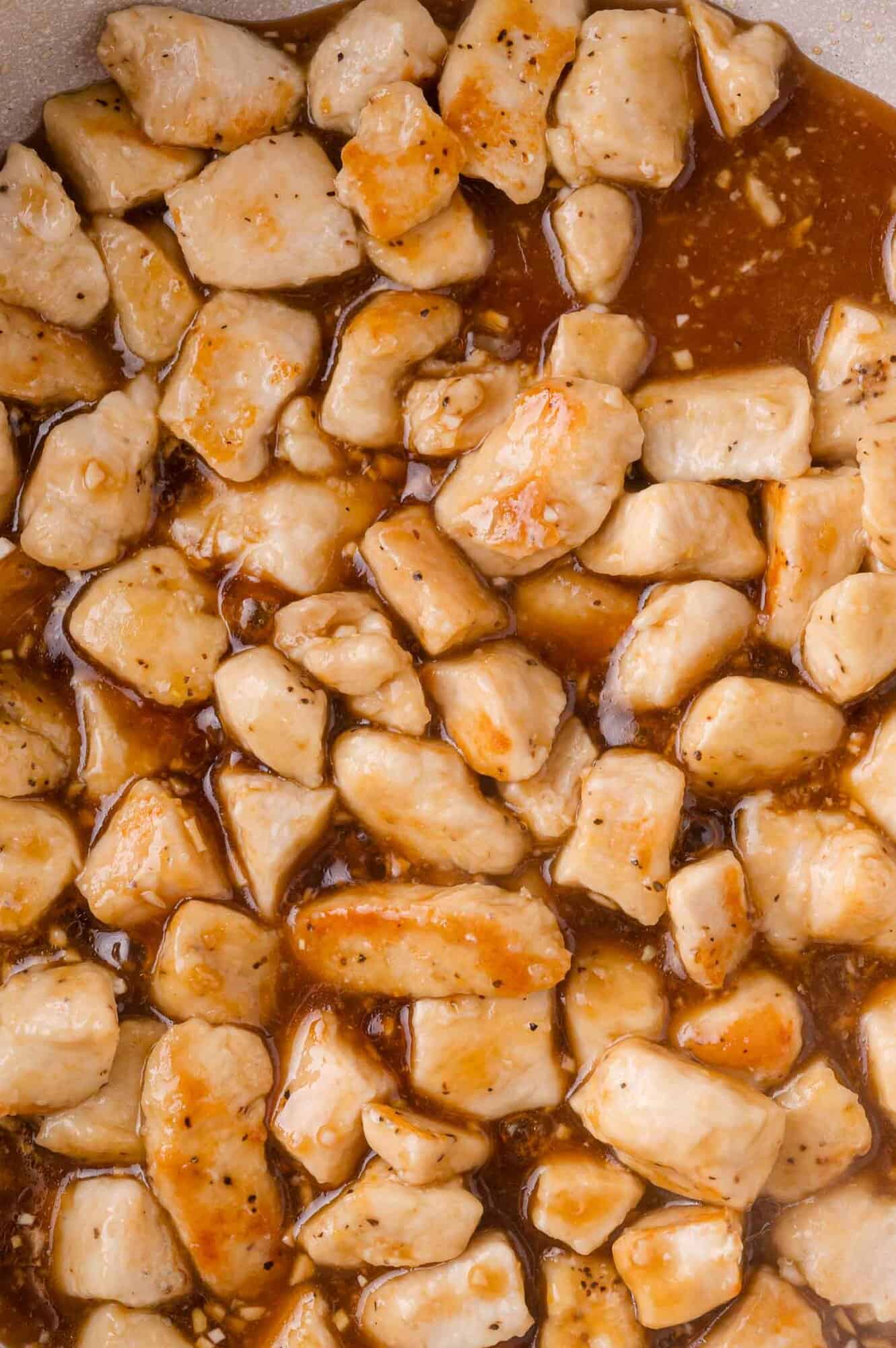 Diced pieces of cooked chicken in a brown teriyaki sauce, filling the frame.
