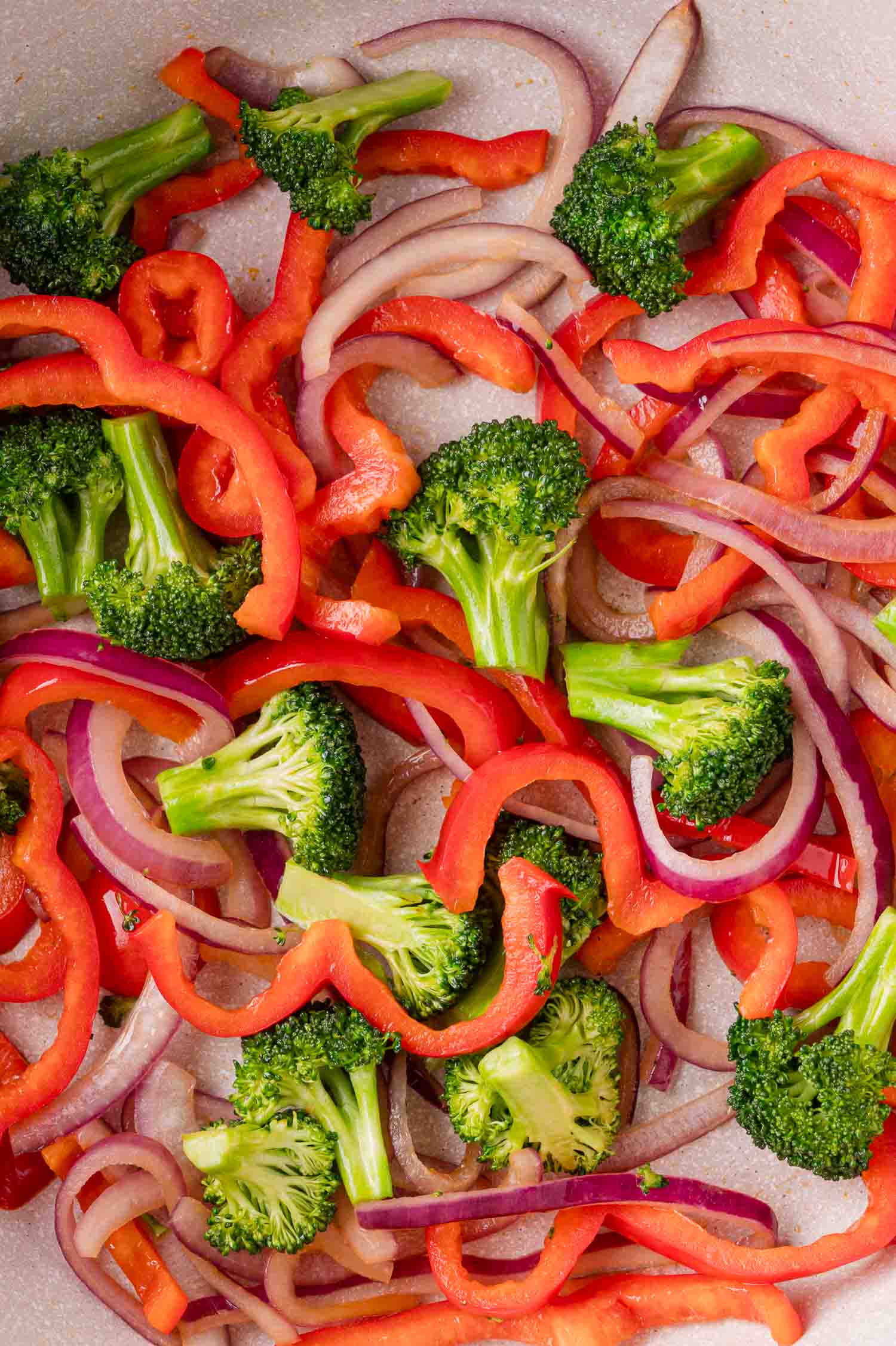 Sliced red bell peppers, broccoli florets, and red onion in a pan.