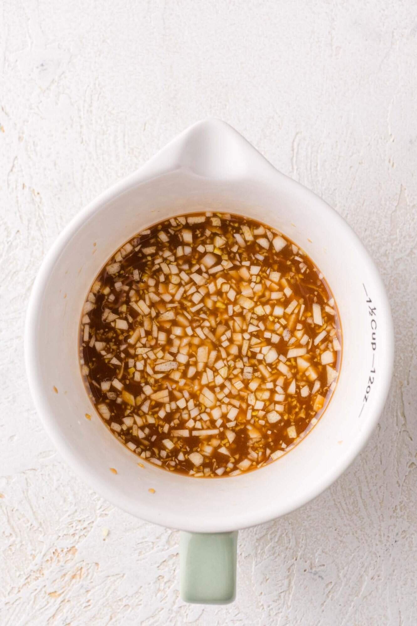 A white measuring cup filled with uncooked teriyaki sauce.
