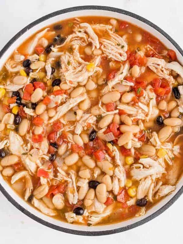 A pot of chicken chili with shredded chicken, white and black beans, corn, and diced tomatoes in broth.