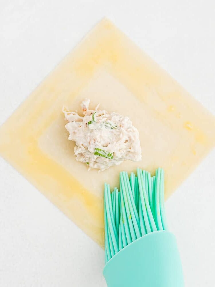 Egg wash being brushed onto a wonton wrapper.