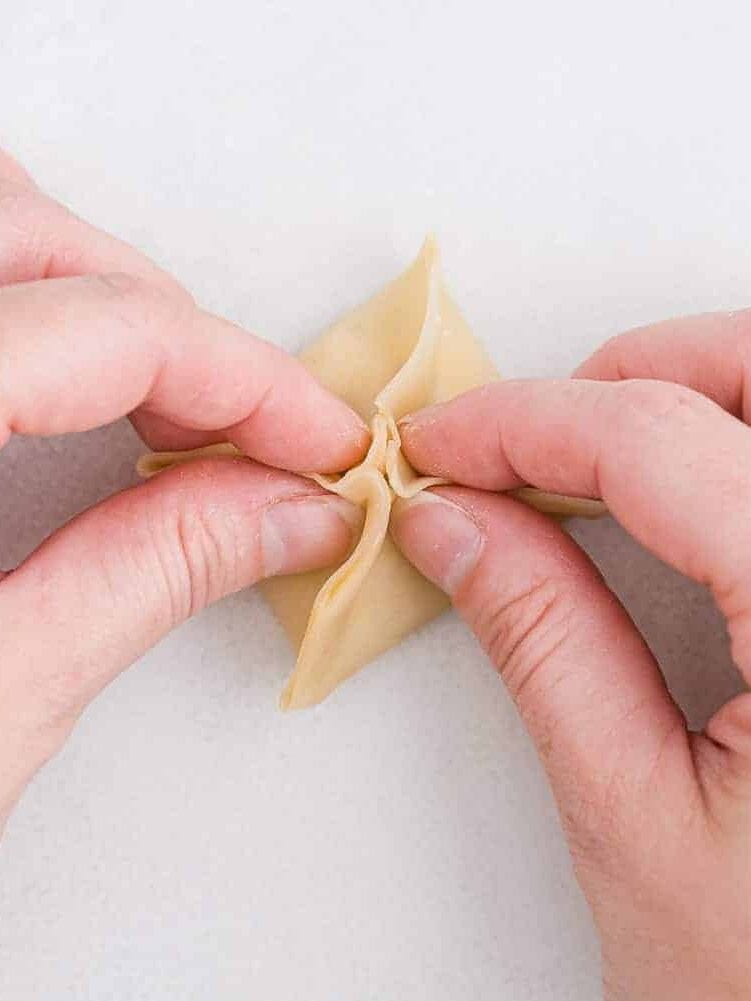 Two hands shown folding a rangoon.