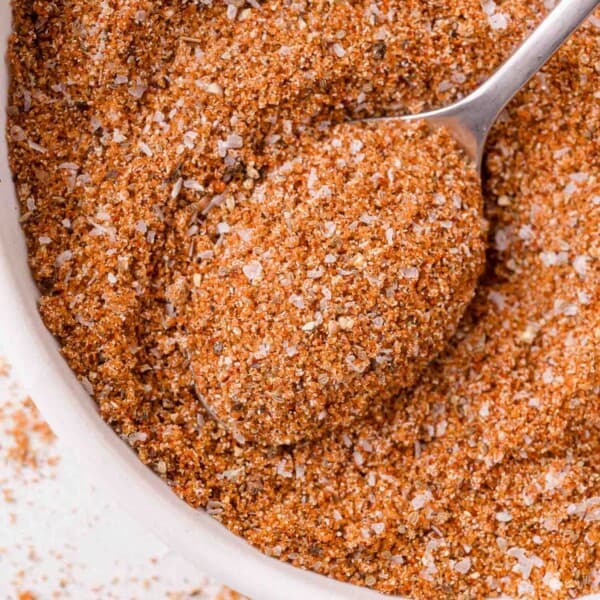 A close-up of a bowl filled with a reddish-brown bbq rub spice mix, with a spoon scooping some of the mixture.