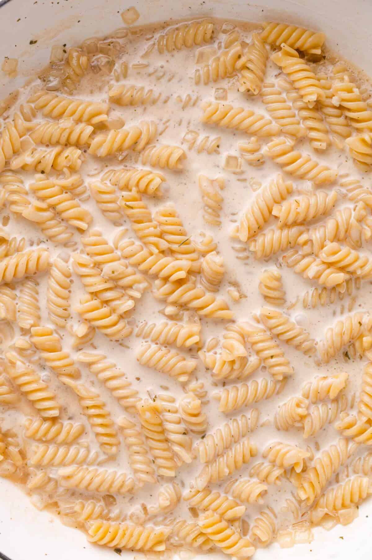 Cooked rotini pasta in a creamy white sauce inside a white pan.