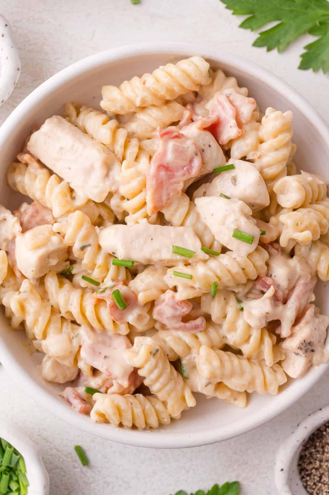 A bowl of creamy rotini pasta with pieces of chicken, bacon, and chopped chives on top.