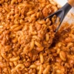 Close-up of a chili mac - a mixture of elbow macaroni, ground meat, beans, and tomato sauce being stirred with a black spatula.