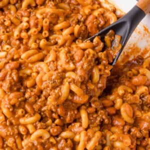 Close-up of a chili mac - a mixture of elbow macaroni, ground meat, beans, and tomato sauce being stirred with a black spatula.