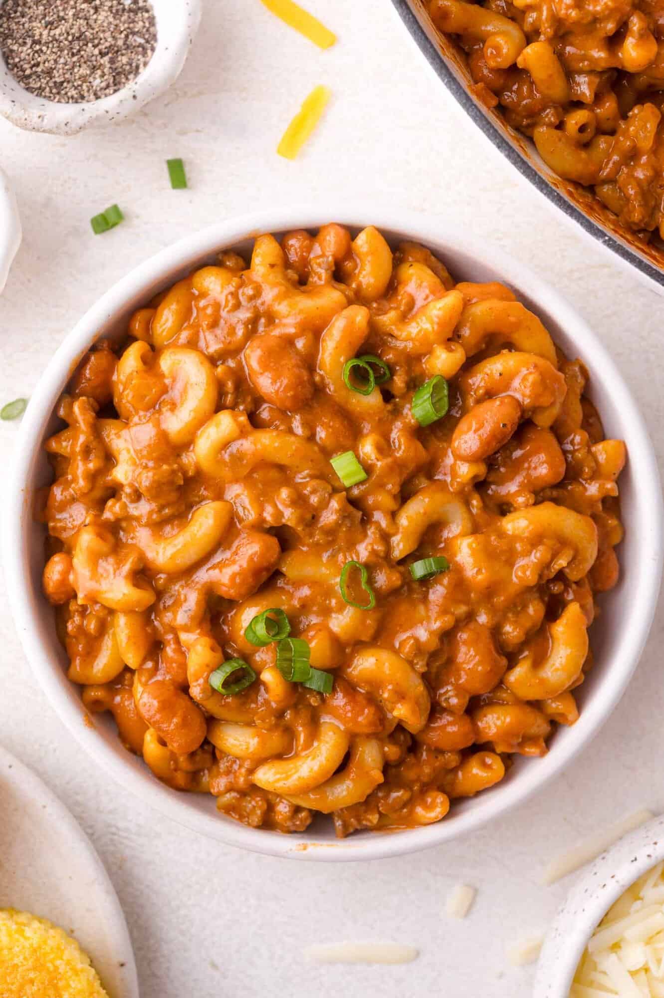 A white bowl filled with macaroni noodles in a thick, meaty tomato sauce, garnished with chopped green onions.