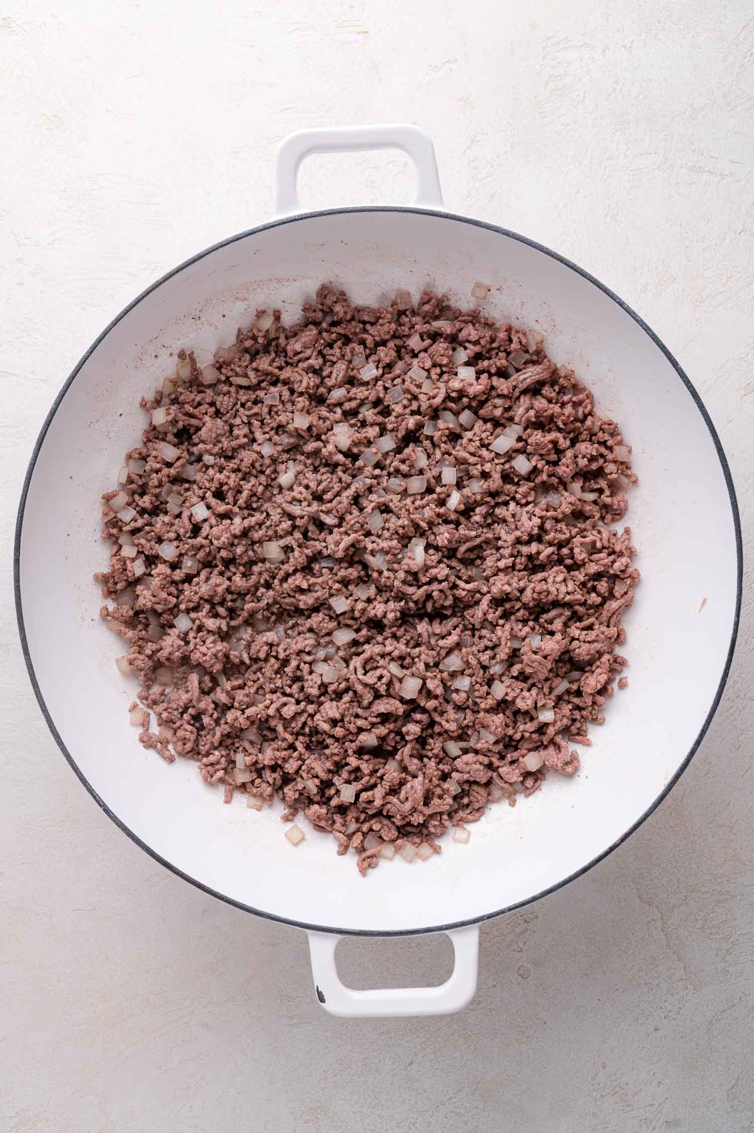 Cooked ground beef and diced onions in a white Dutch oven, viewed from above.