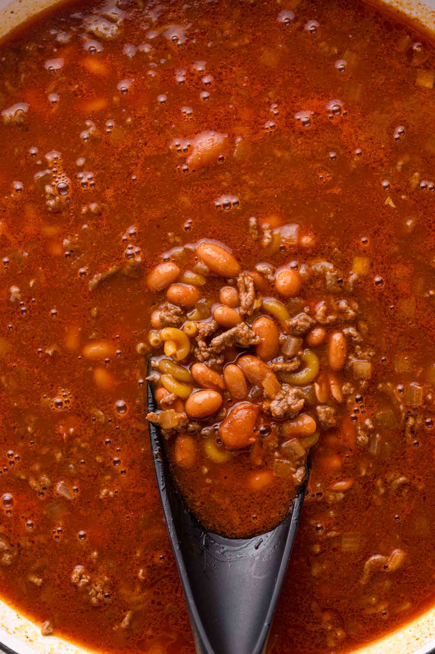 Close-up of a spoon scooping chili with ground beef, beans, and a tomato-based broth.