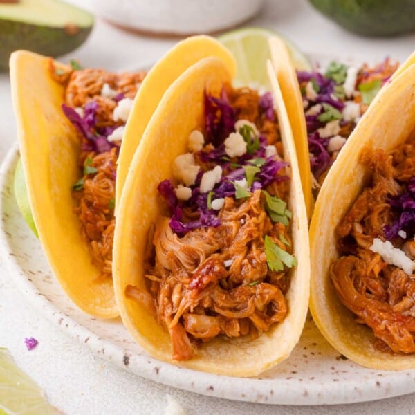 Three corn tortillas filled with shredded chipotle chicken, topped with chopped purple cabbage, cilantro, and crumbled cheese, served on a white plate.