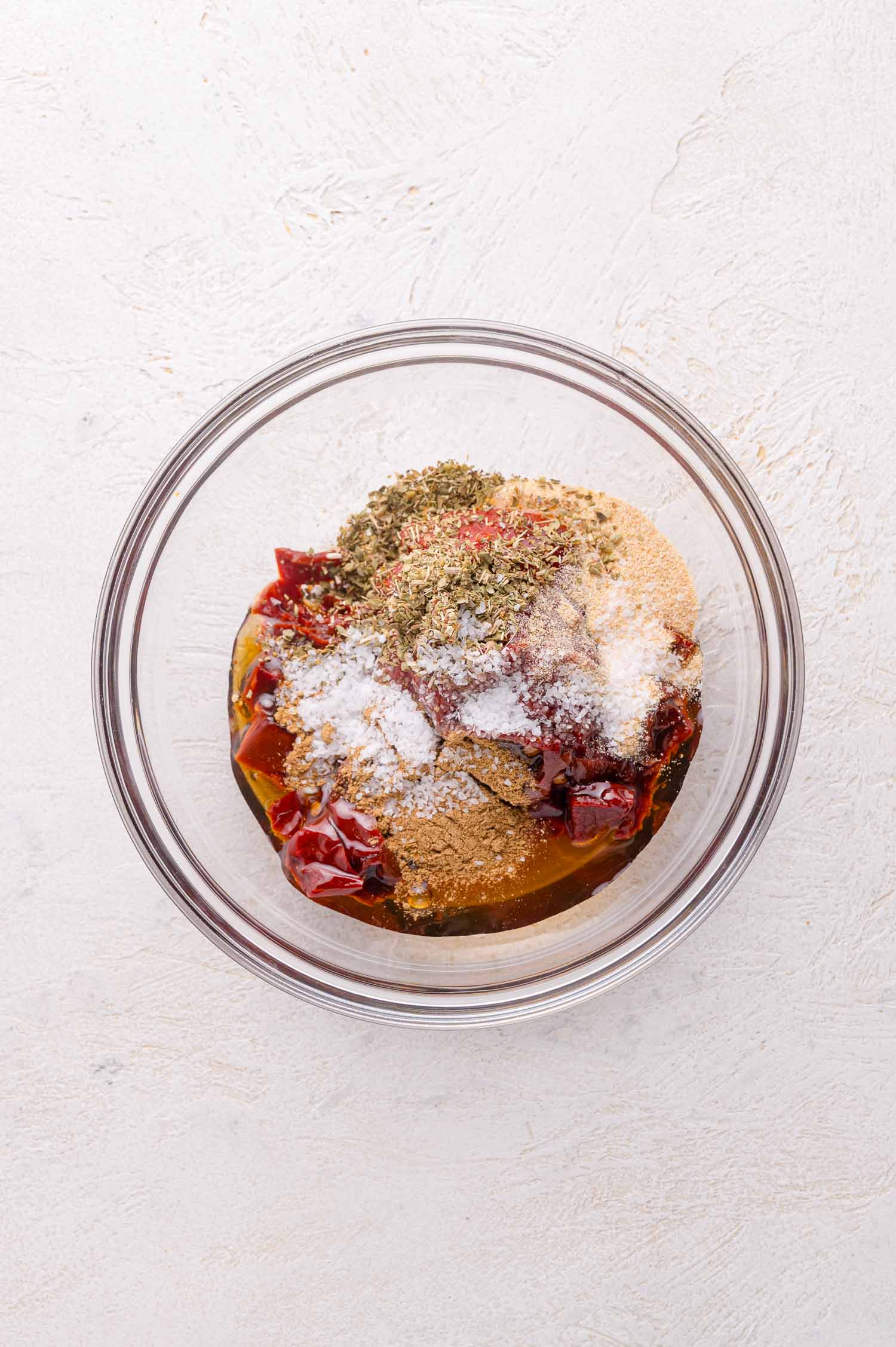 A glass bowl containing sauce ingredients on a white surface.