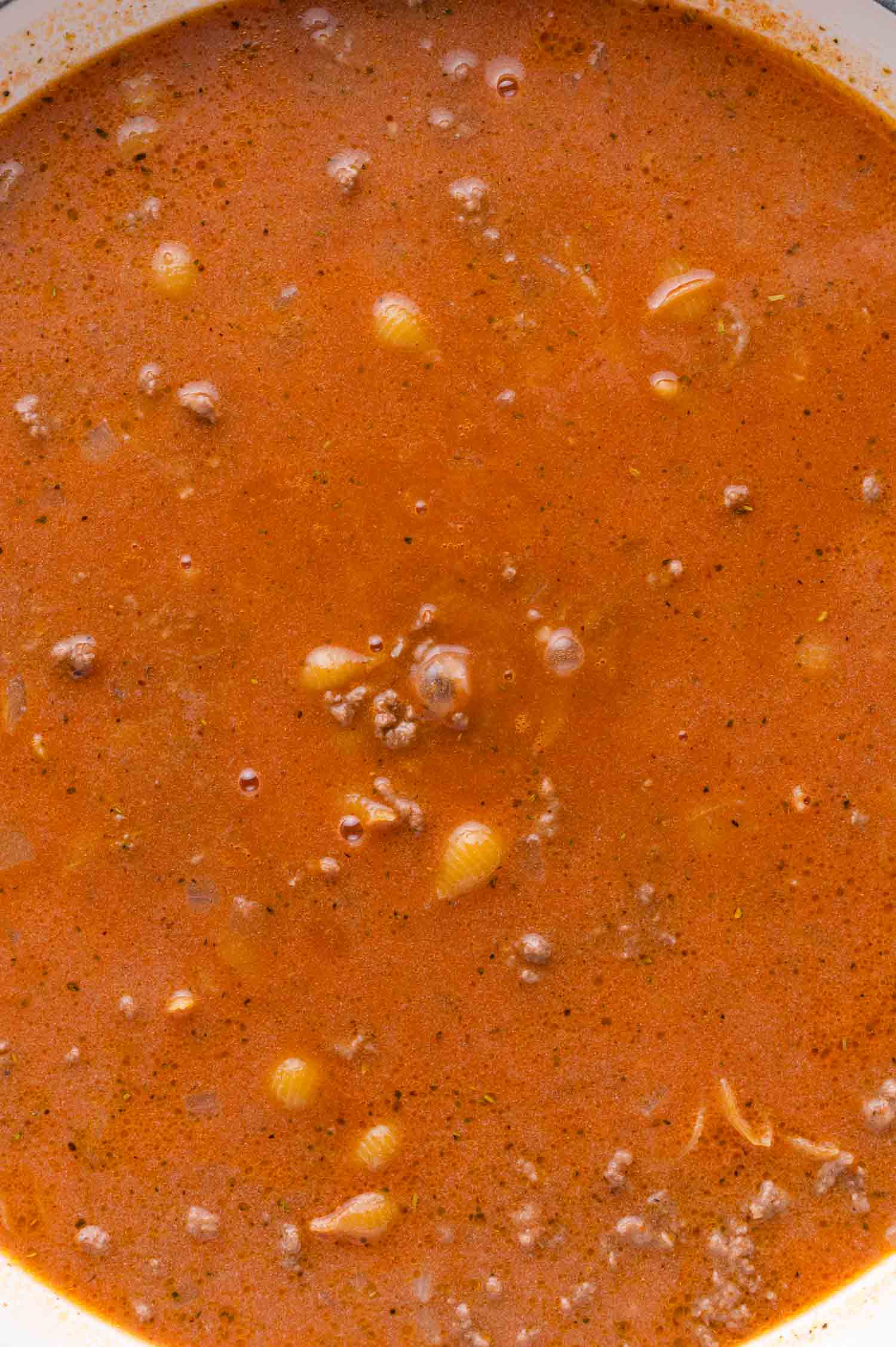 A close-up of creamy tomato sauce with ground beef and small pasta shells, with visible herbs and seasonings.
