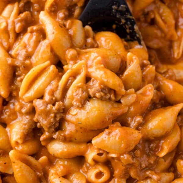 Close-up of cooked pasta shells mixed with ground beef and a creamy tomato sauce, being stirred with a black spoon.