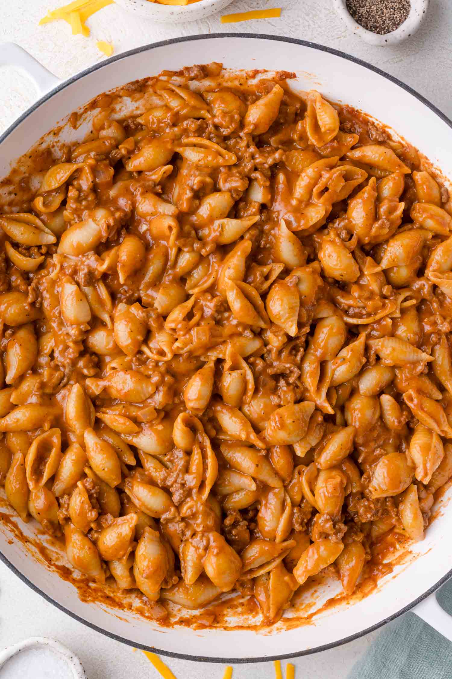 Pasta shells mixed with ground beef and a creamy, tomato-based sauce in a large white skillet.