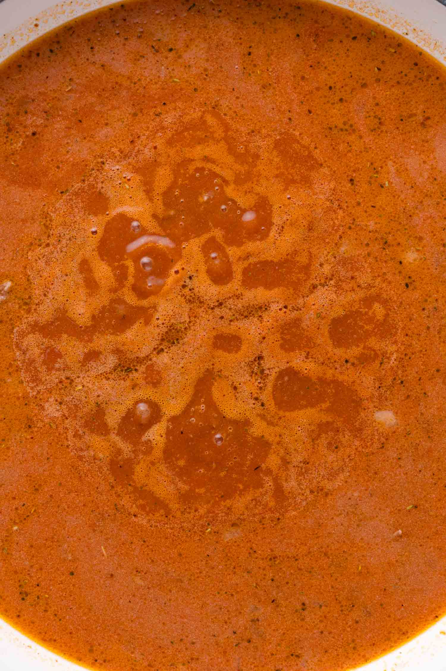 Close-up of a pan filled with reddish-brown tomato sauce with visible oil and spice on the surface.