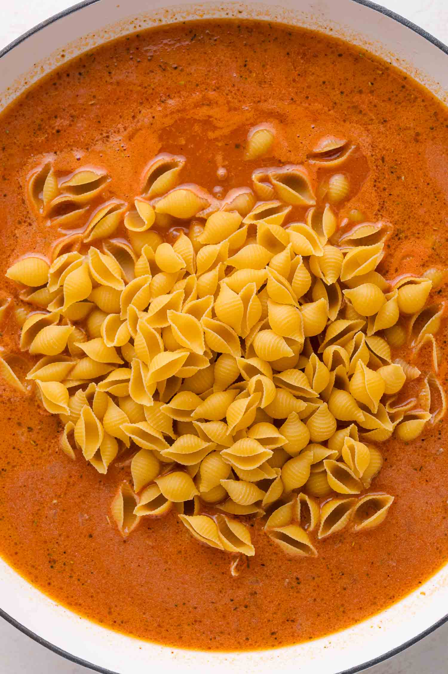 Uncooked shell pasta is added to a pot of creamy tomato sauce.