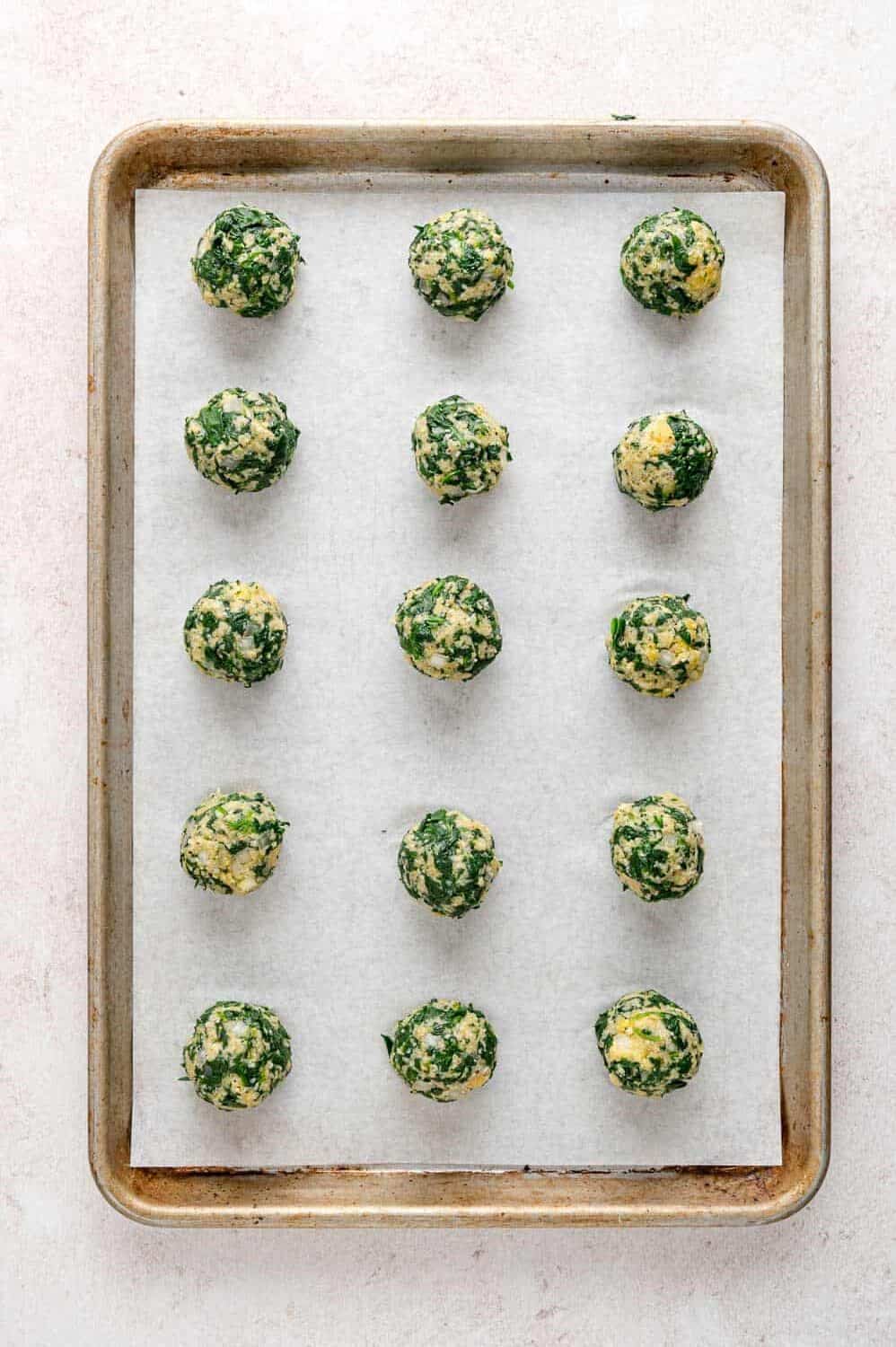 Unbaked spinach balls on a parchment-lined baking sheet.