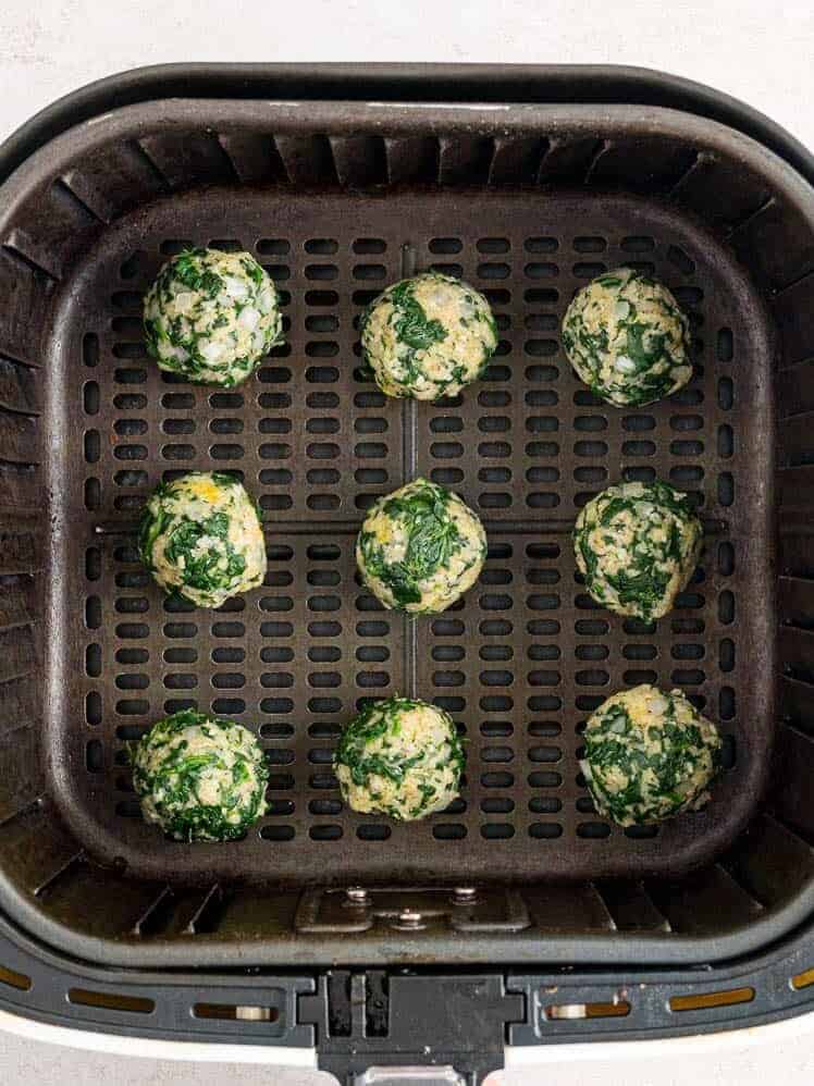 Uncooked spinach balls arranged inside the basket of an air fryer.