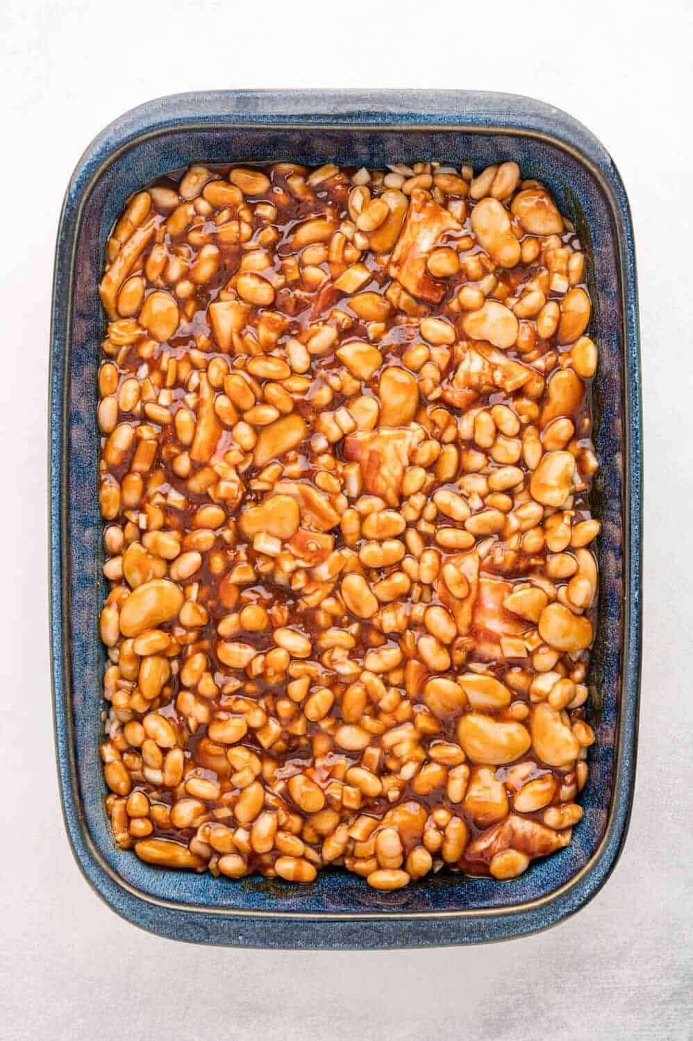 A blue rectangular baking dish filled with baked beans in a thick, brown sauce, viewed from above.