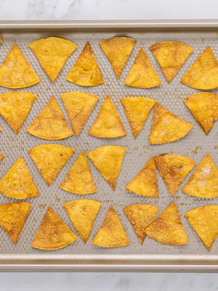 Baked tortilla chips on a baking sheet.