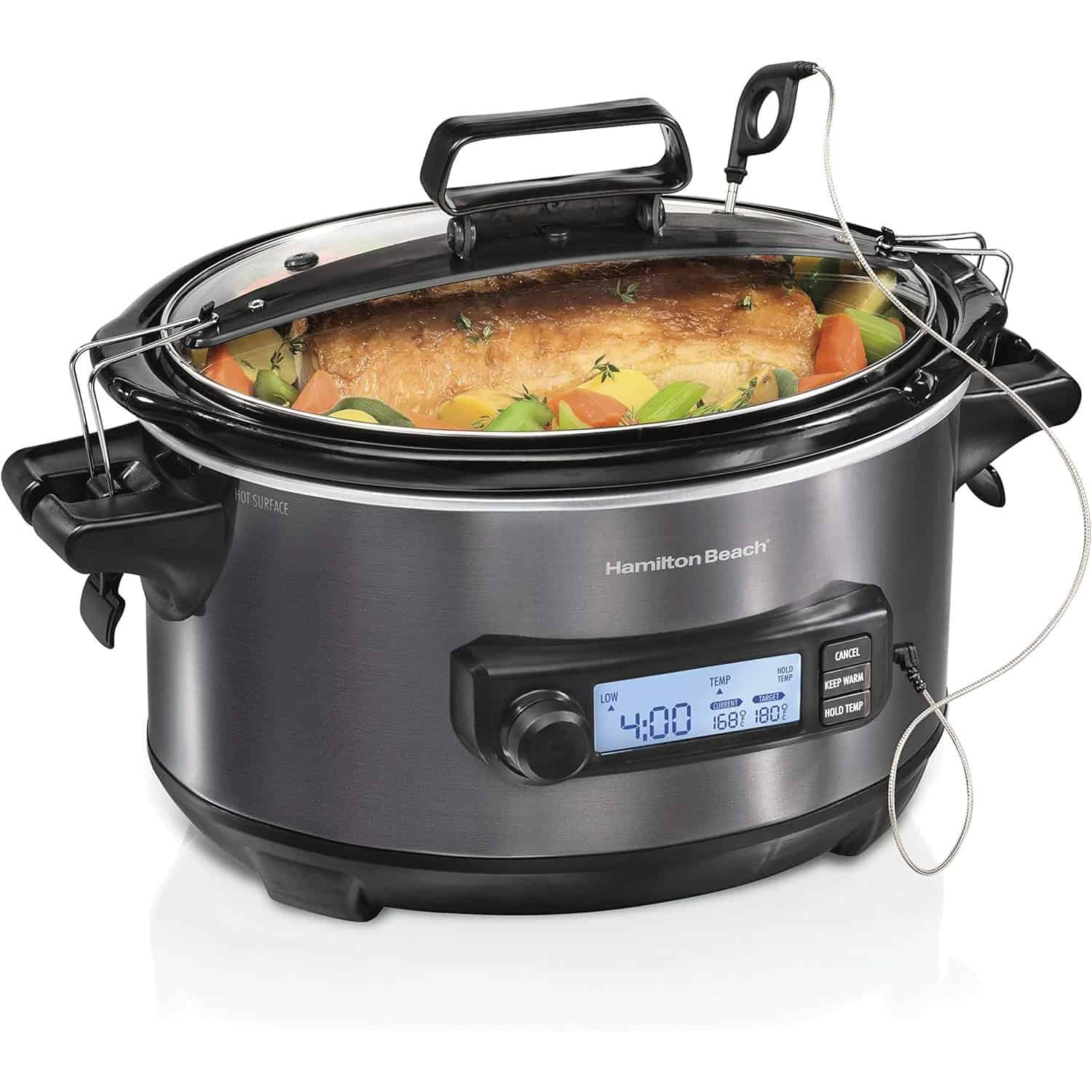 A stainless steel Hamilton Beach slow cooker with a digital display, cooking a roast with vegetables inside, and a built-in meat thermometer probe attached.
